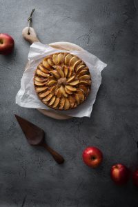 An apple cake on a blue stone surface with fresh apples and cake server.