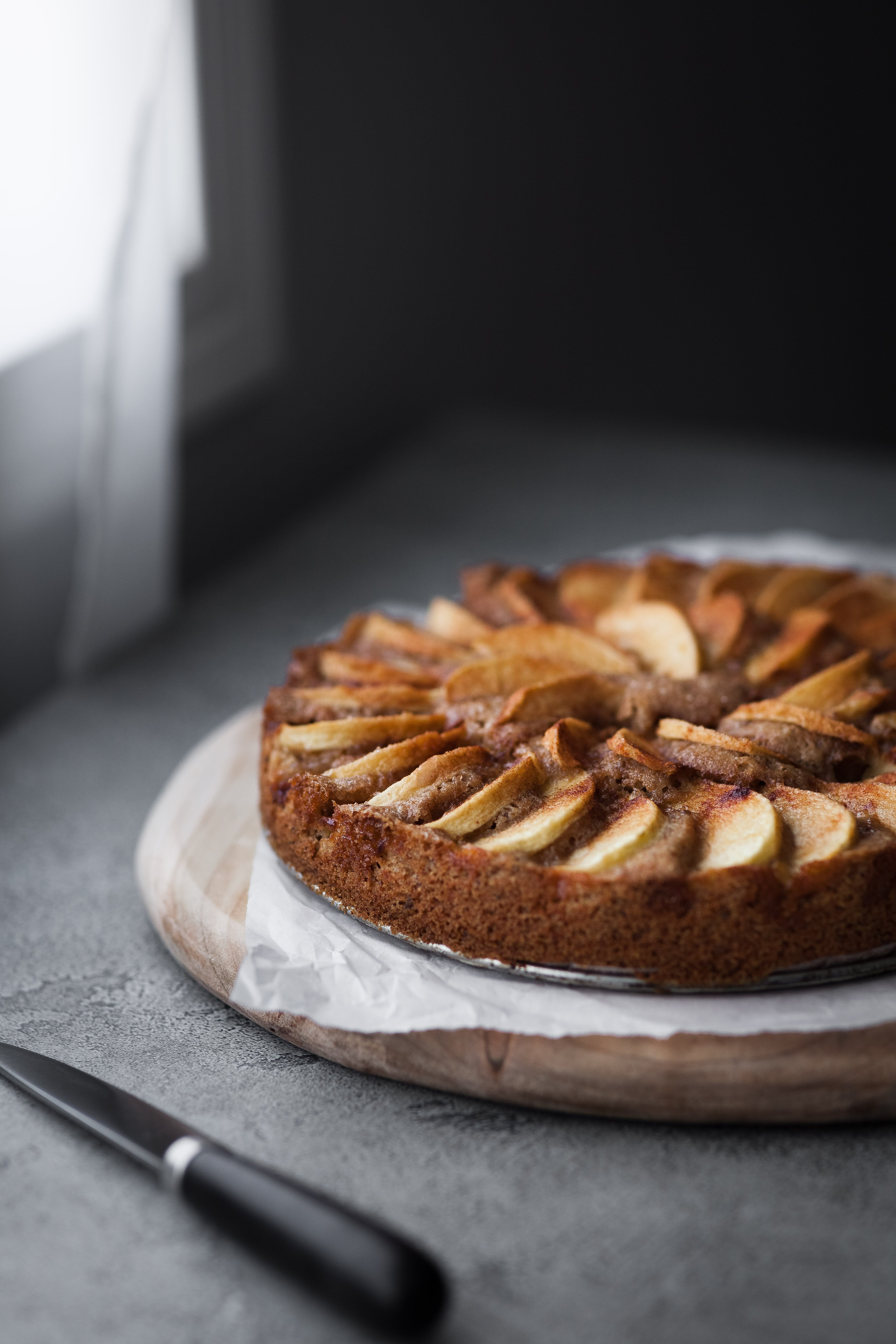 a ¾ angle view of a vegan german apple cake sitting beside a window with a knife in the foreground.