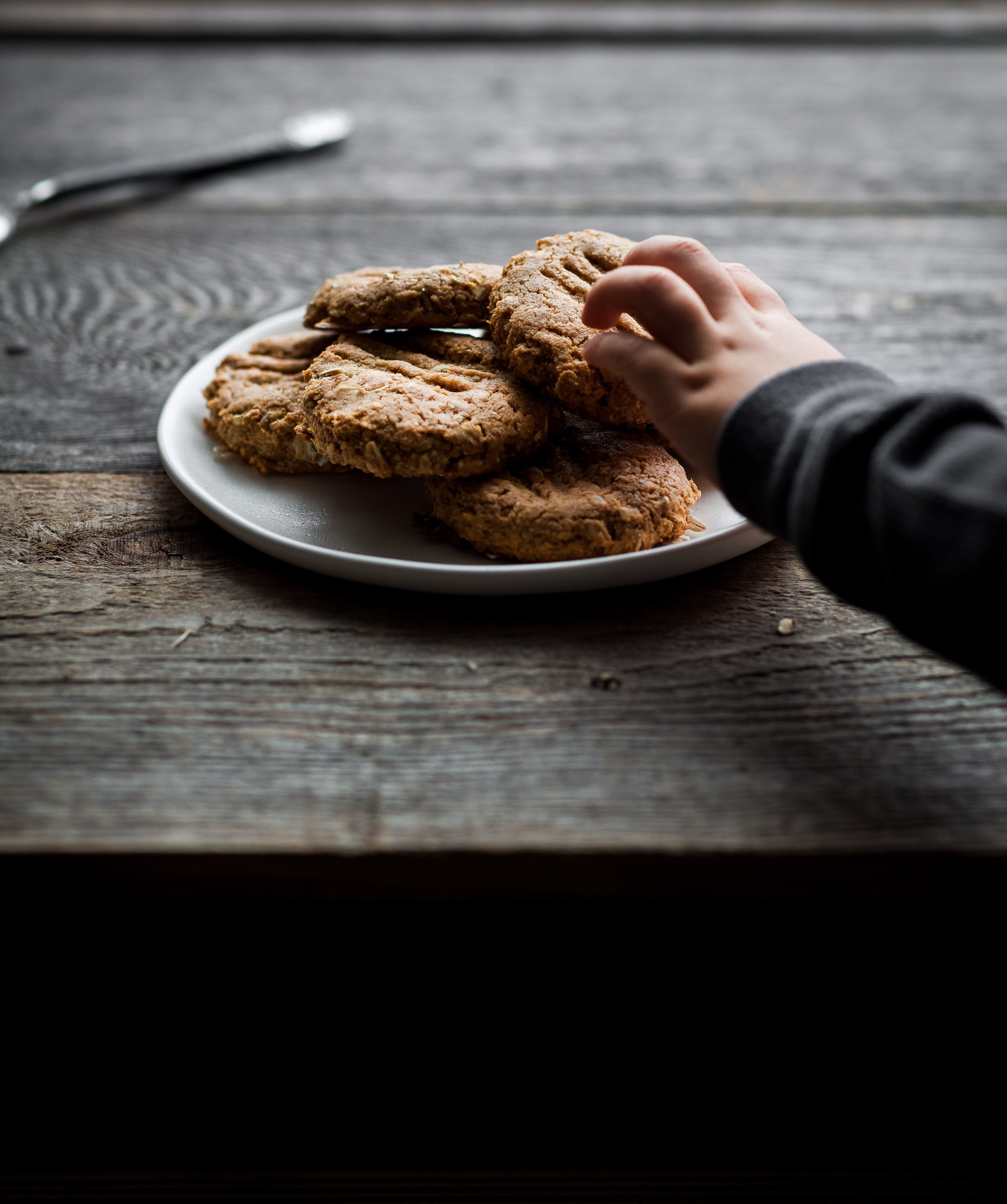a hand reaching for a plate of vegan peanut butter cookies.