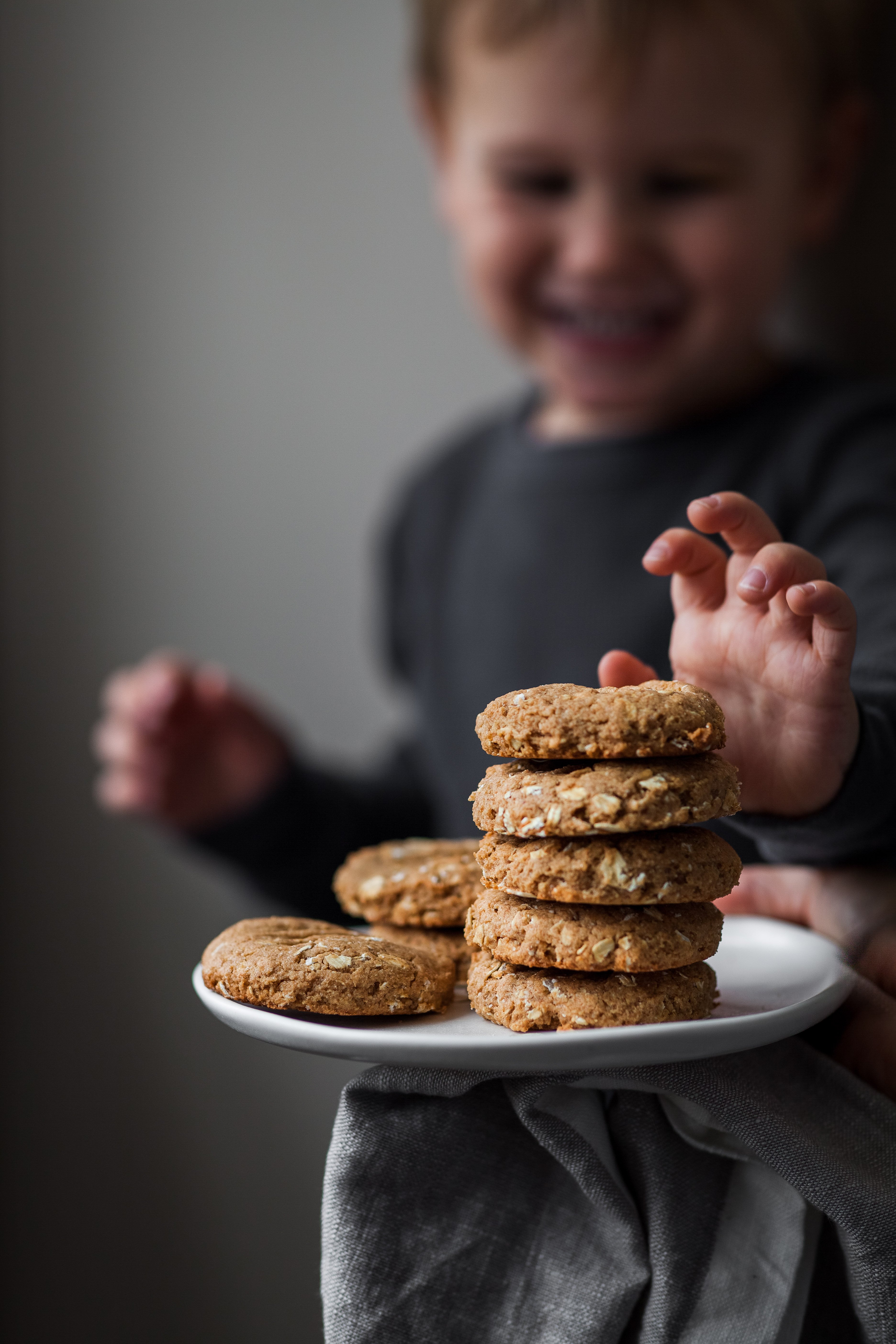 a small child reaching for a peanut butter oatmeal cookie on a plate.