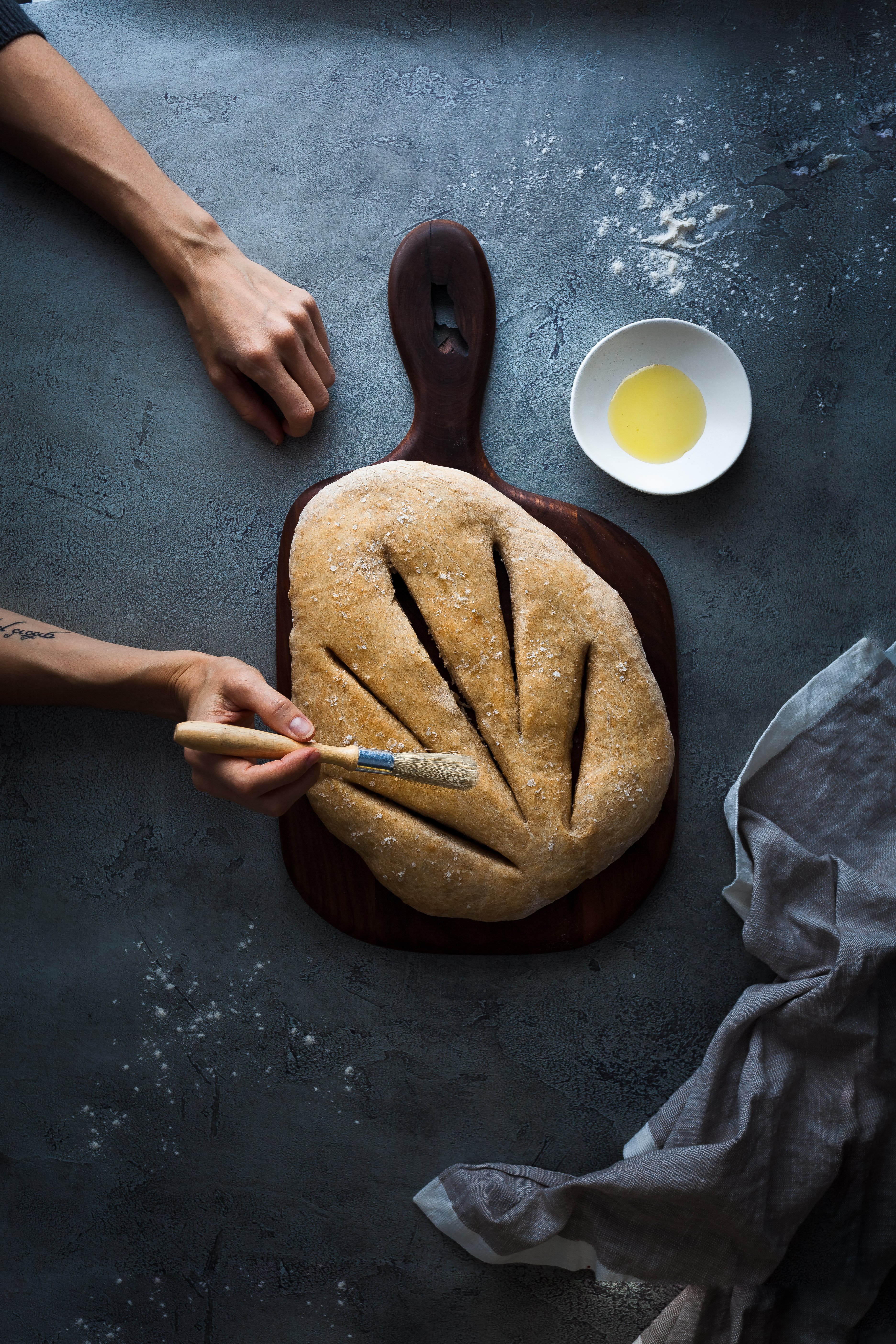 an overhead image of a person basting baked fougasse with olive oil.