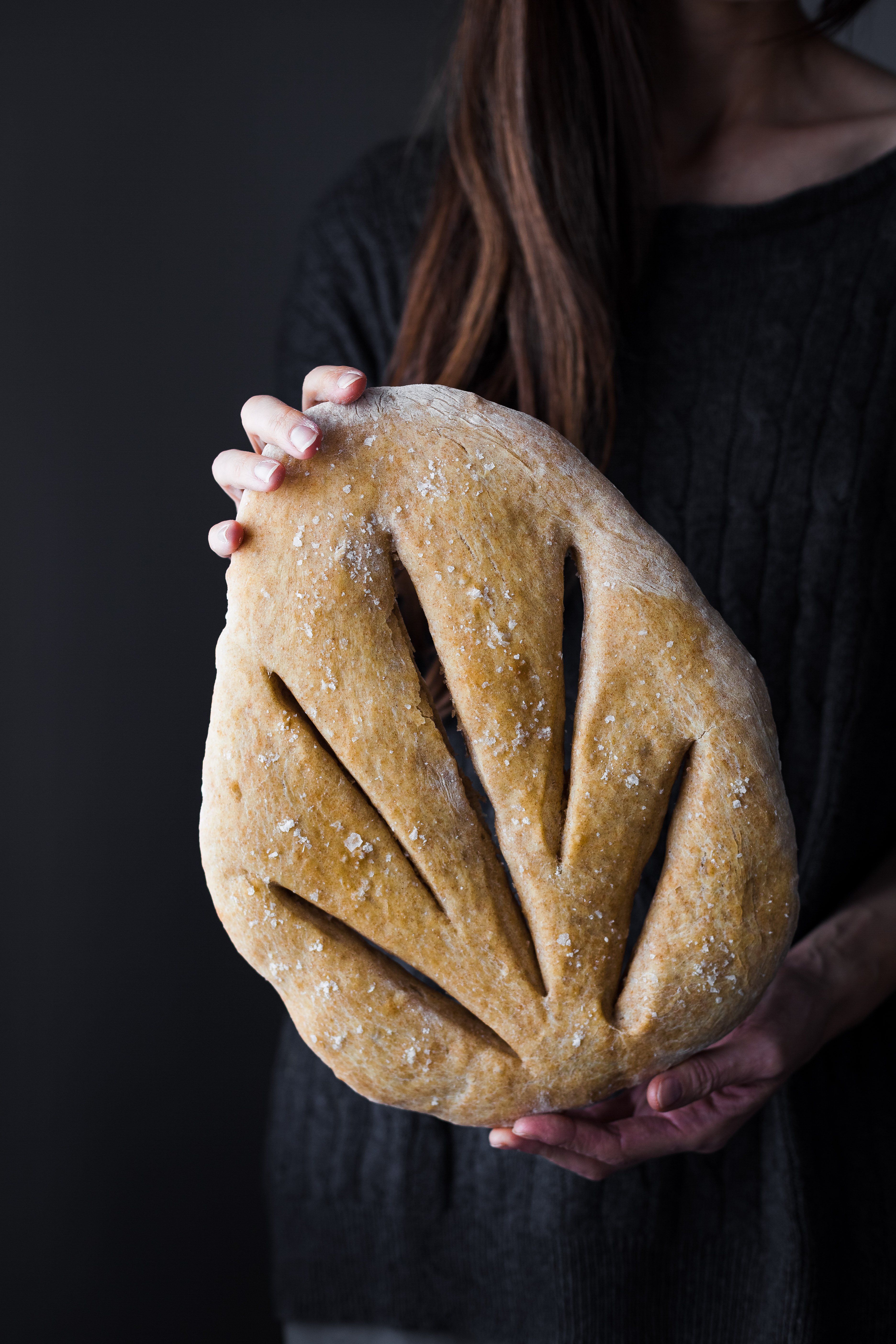 A head on image of a person holding a loaf of No Knead Garlic Fougasse bread.