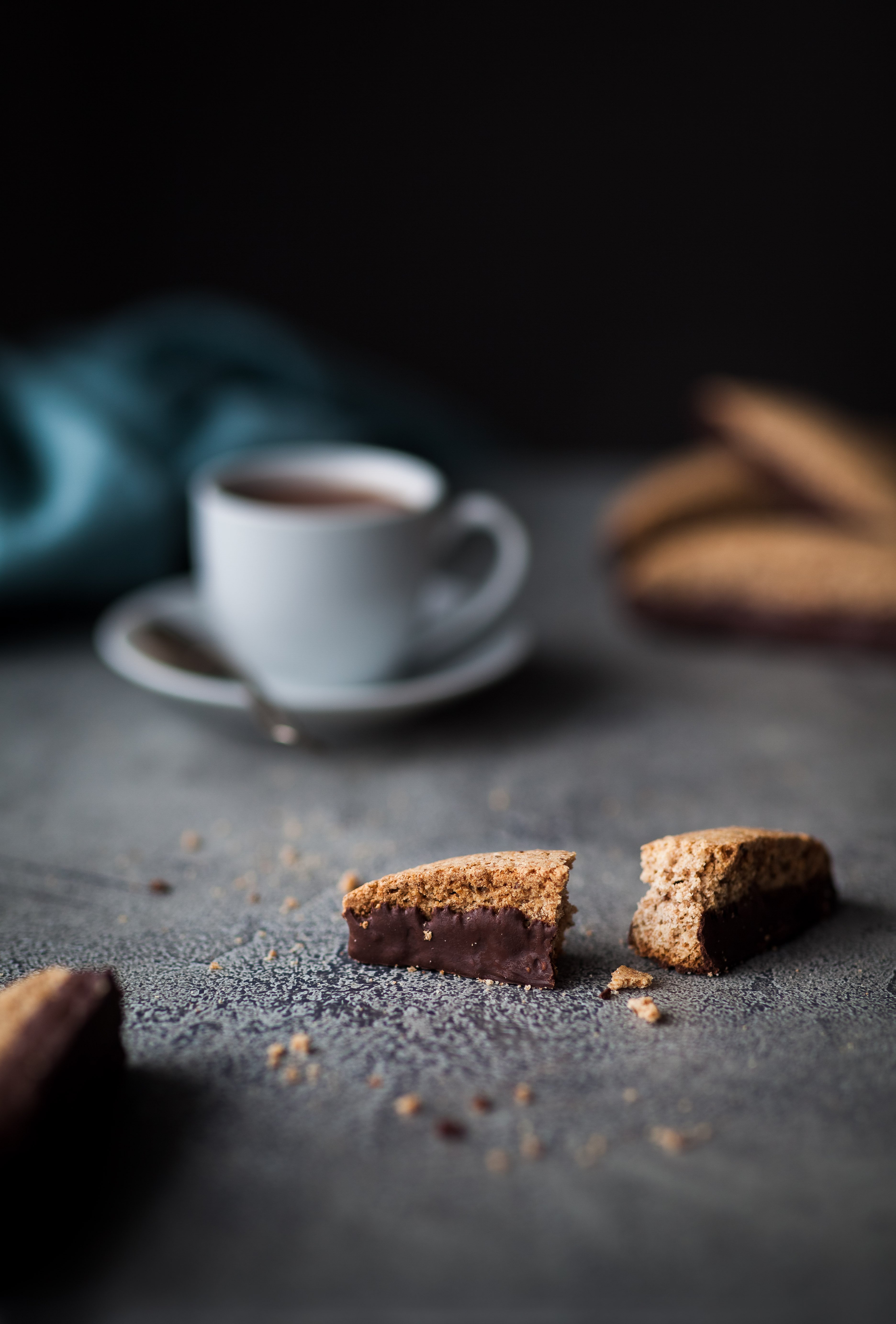 head on image of a biscotti cookie broken in half with a white cup of espresso in the background.