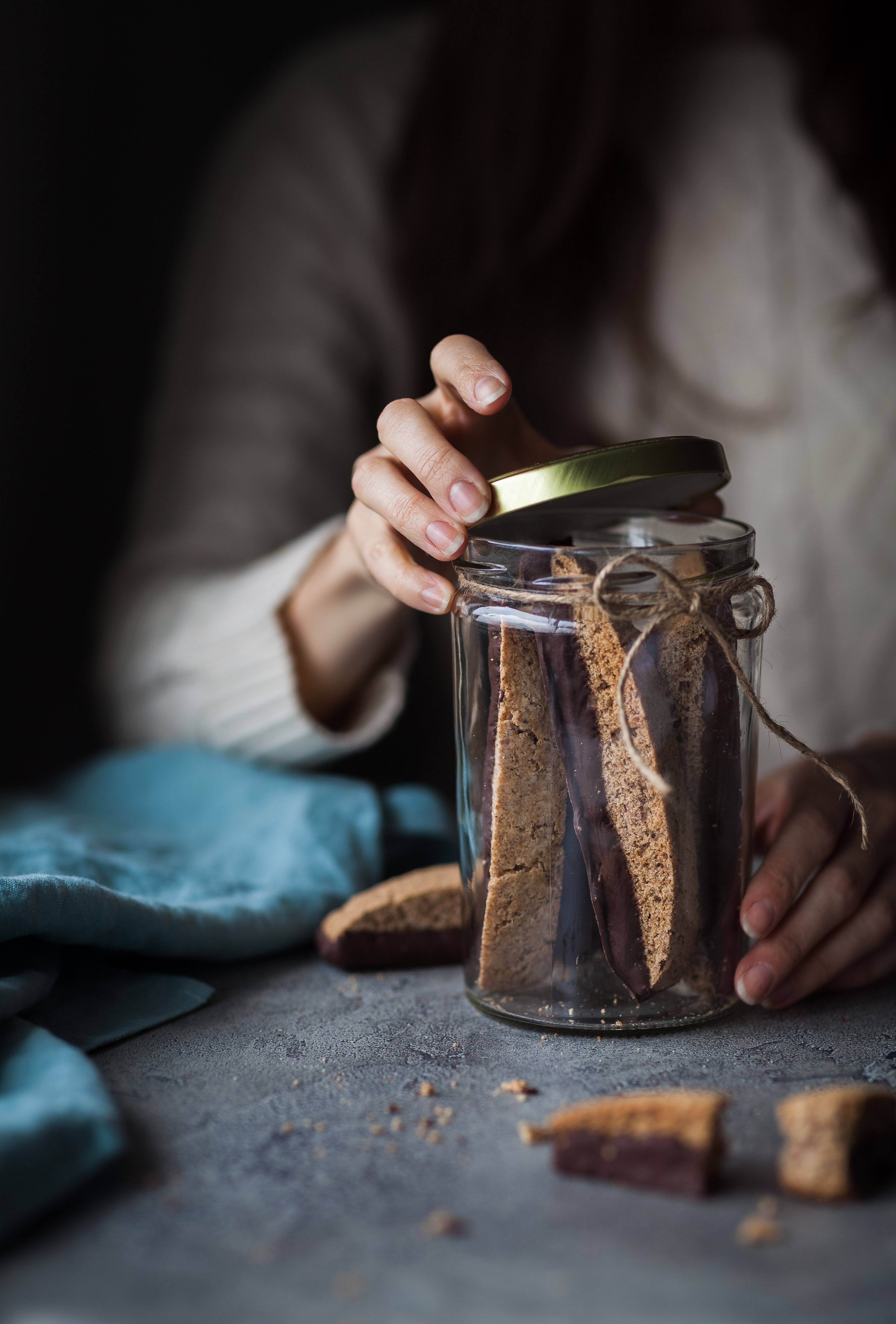 a person opeing a jar of vegan chocolate olive oil biscotti cookies.