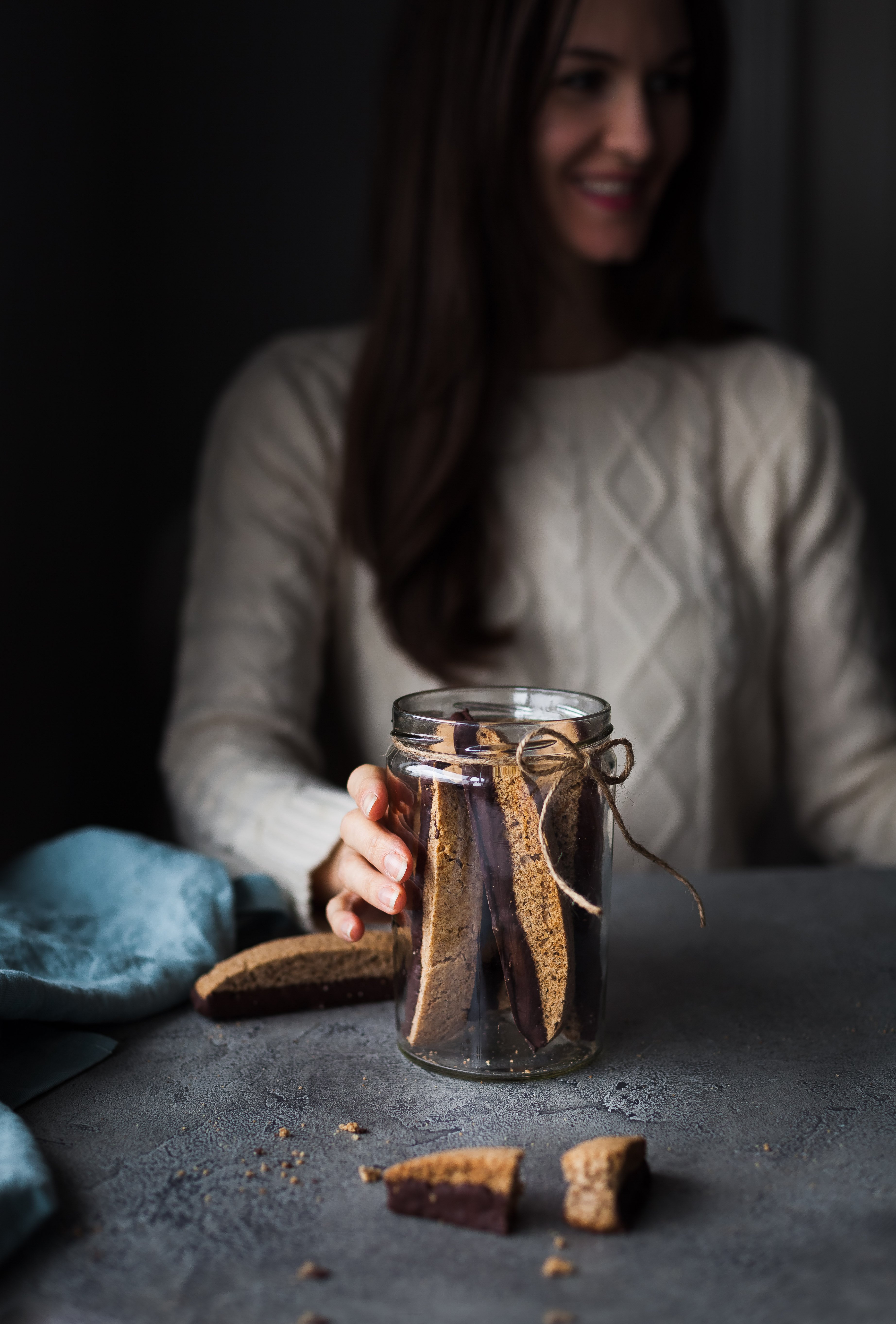 a person holding a jar of vegan chocolate olive oil biscotti with a twine bow on it.