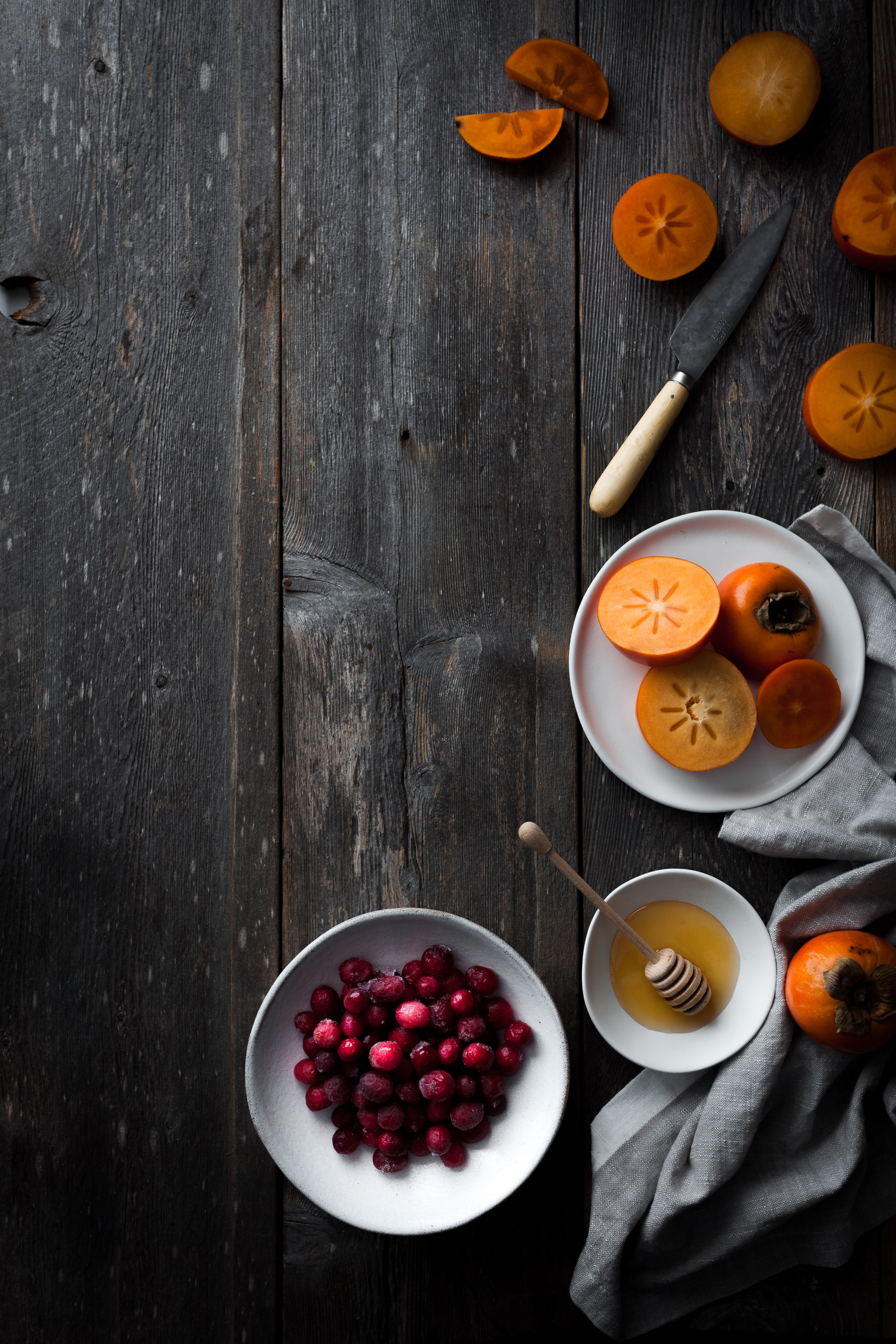 sliced persimmons and cranberries on a wooden surface.