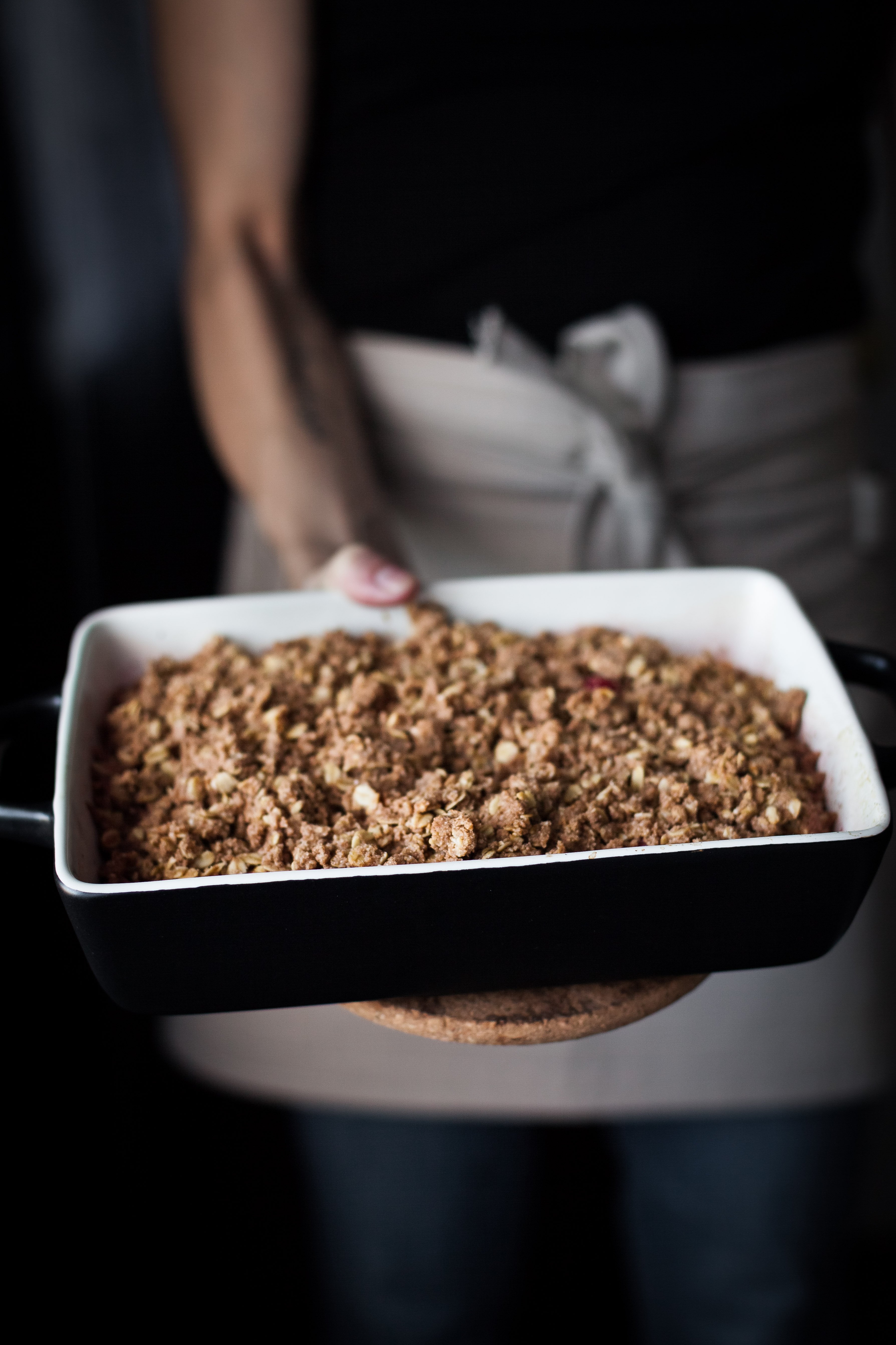 a baker holding a cranberry crisp in a black baking dish.