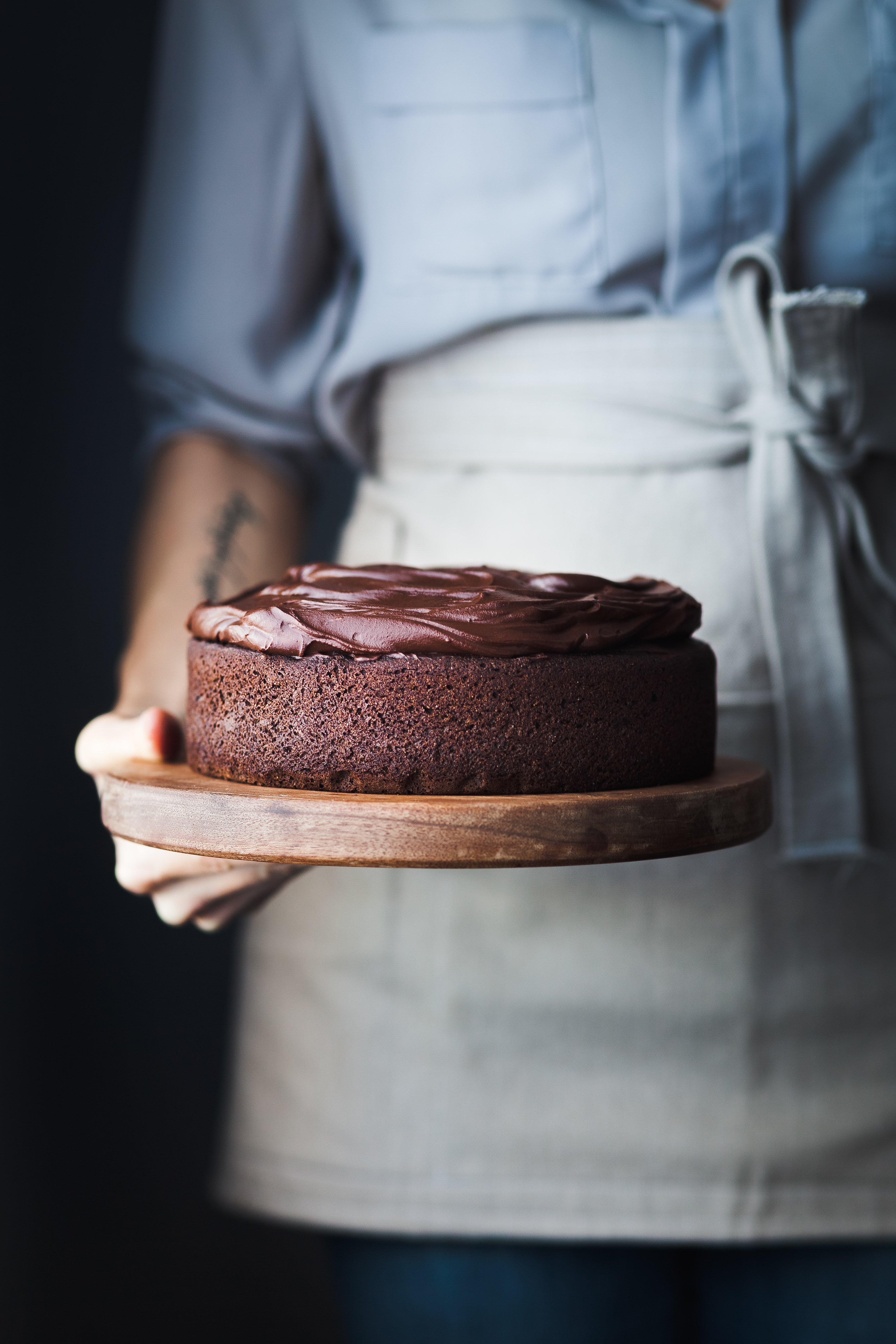 a head on image of a baker holding a Double Chocolate Beetroot Cake on a wooden cutting board.