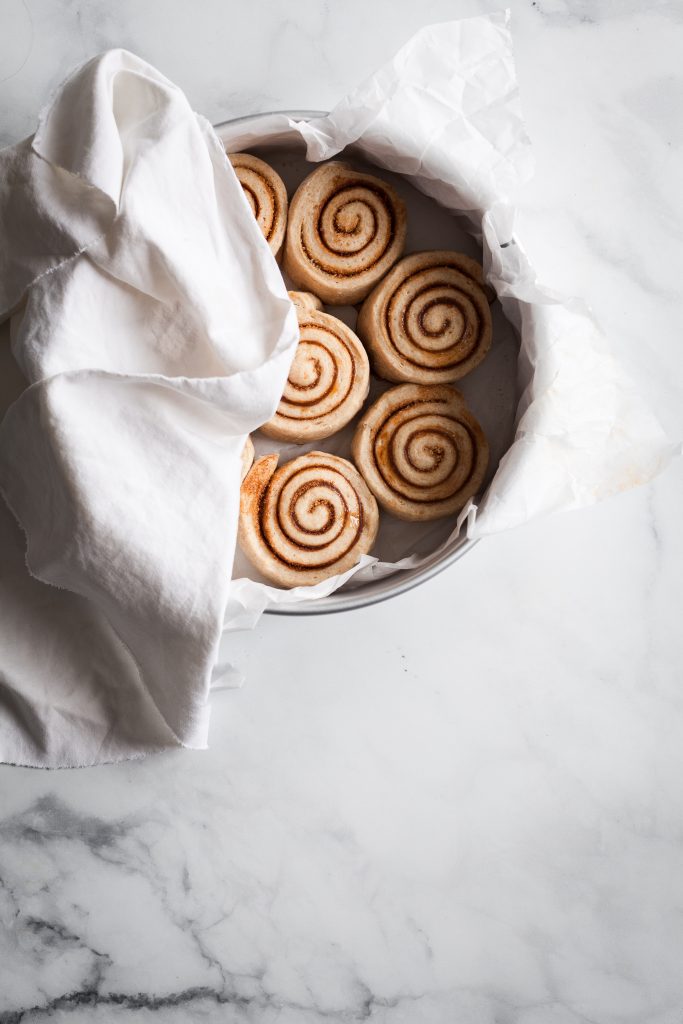 Overhead shot of Vegan Cinnamon Rolls rising in a pan half covered with a linen towel. 