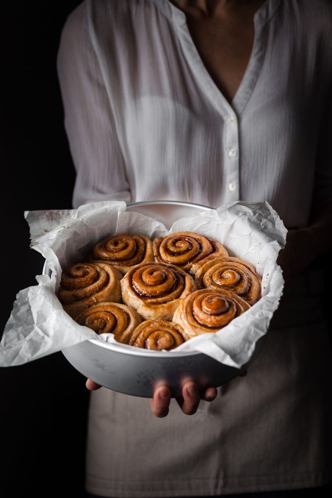 a head on image of a baker holding a pan of cinnamon rolls.