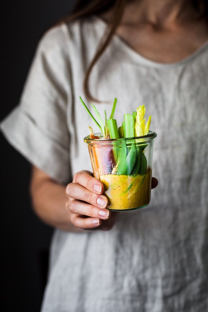 A head on image of a person holding cup of veggies and gold dip in a glass jar.