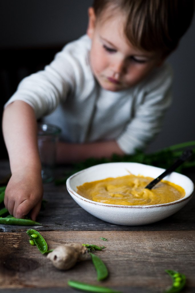 A head on image of a child reaching for peas with a bowl of dip off to the side.