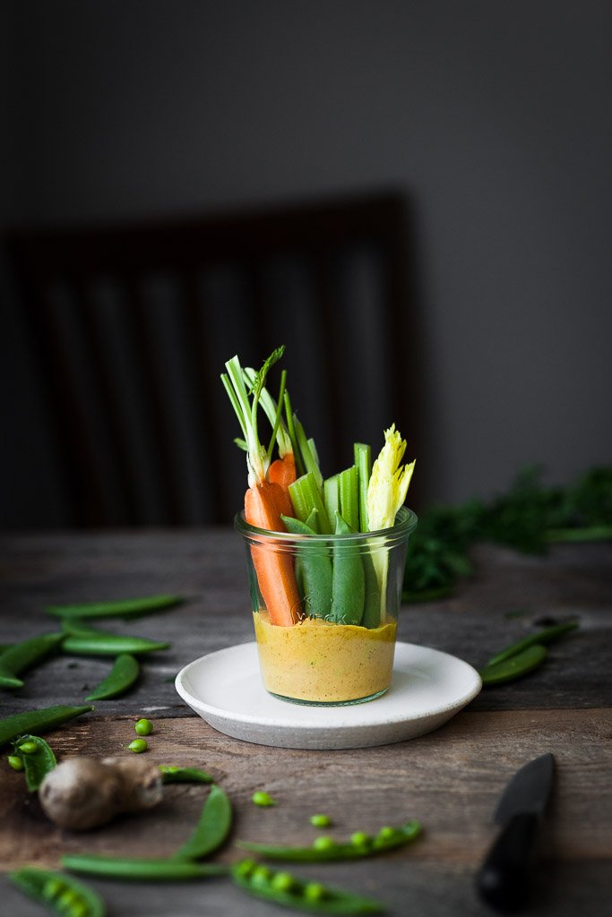 A head on image of a jar of gold dip with veggies.