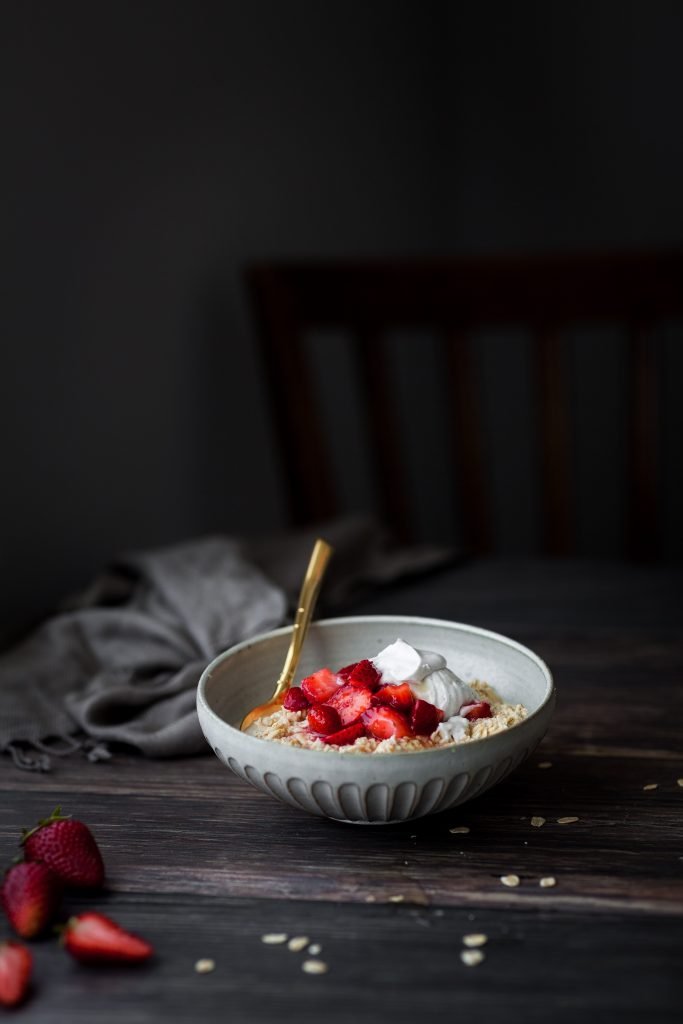 a head on view of a bowl of strawberry bircher museli on a wood surface with a linen.