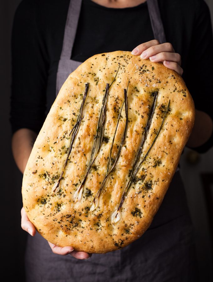 a head on image of a baker holding a loaf of focaccia bread.