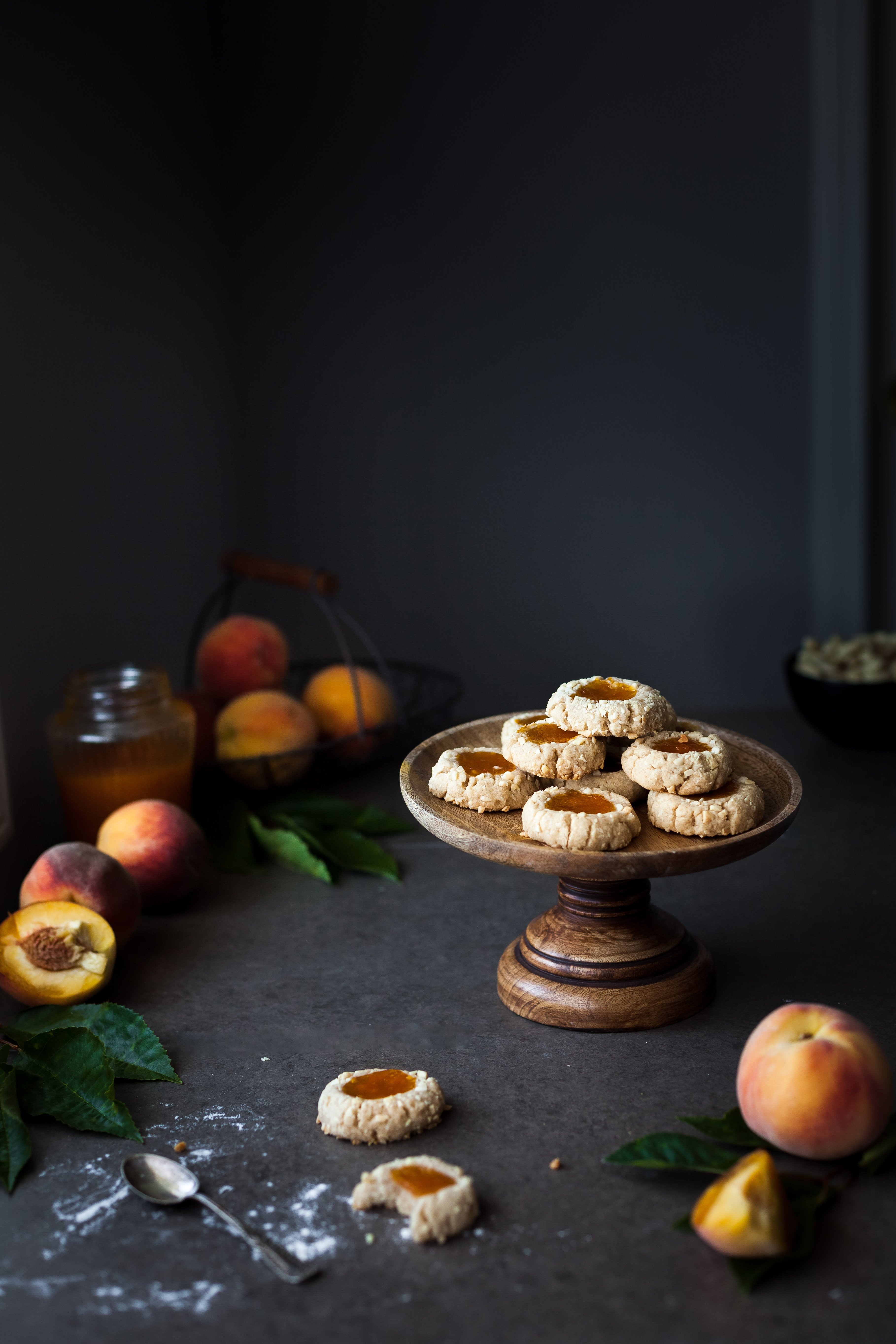 a head on image of a cookie stand with thumbprint cookies ontop with peaches and jam in the background.