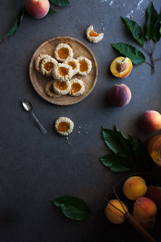 overhead image of vegan thumbprint cookies sitting on a blue backdrop with peaches. 
