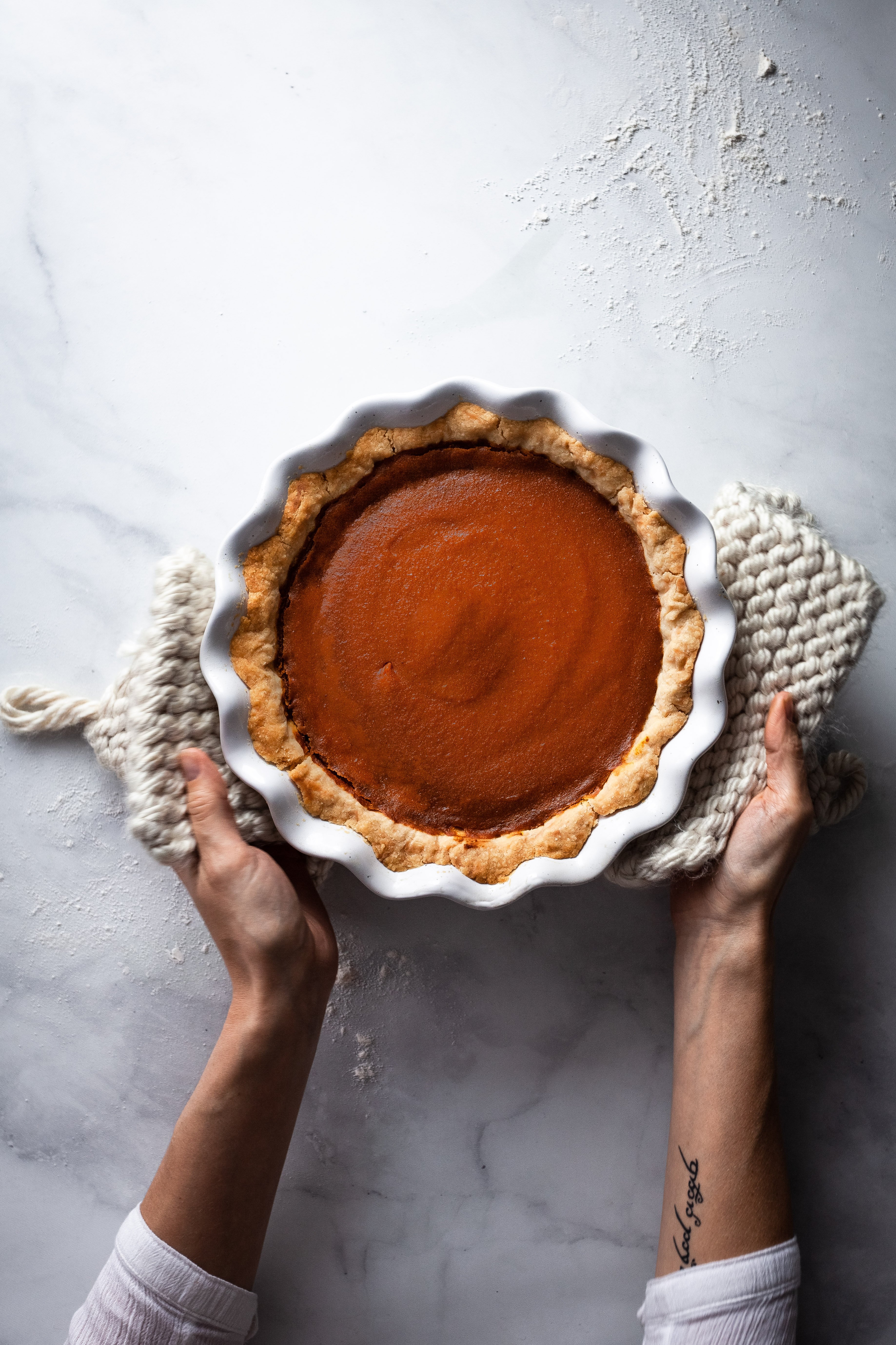 overhead image of vegan pumpkin pie with a baker holding it with two hands.