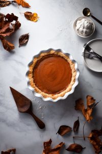 overhead image of vegan pumpkin pie with leaves and a pie lifter.