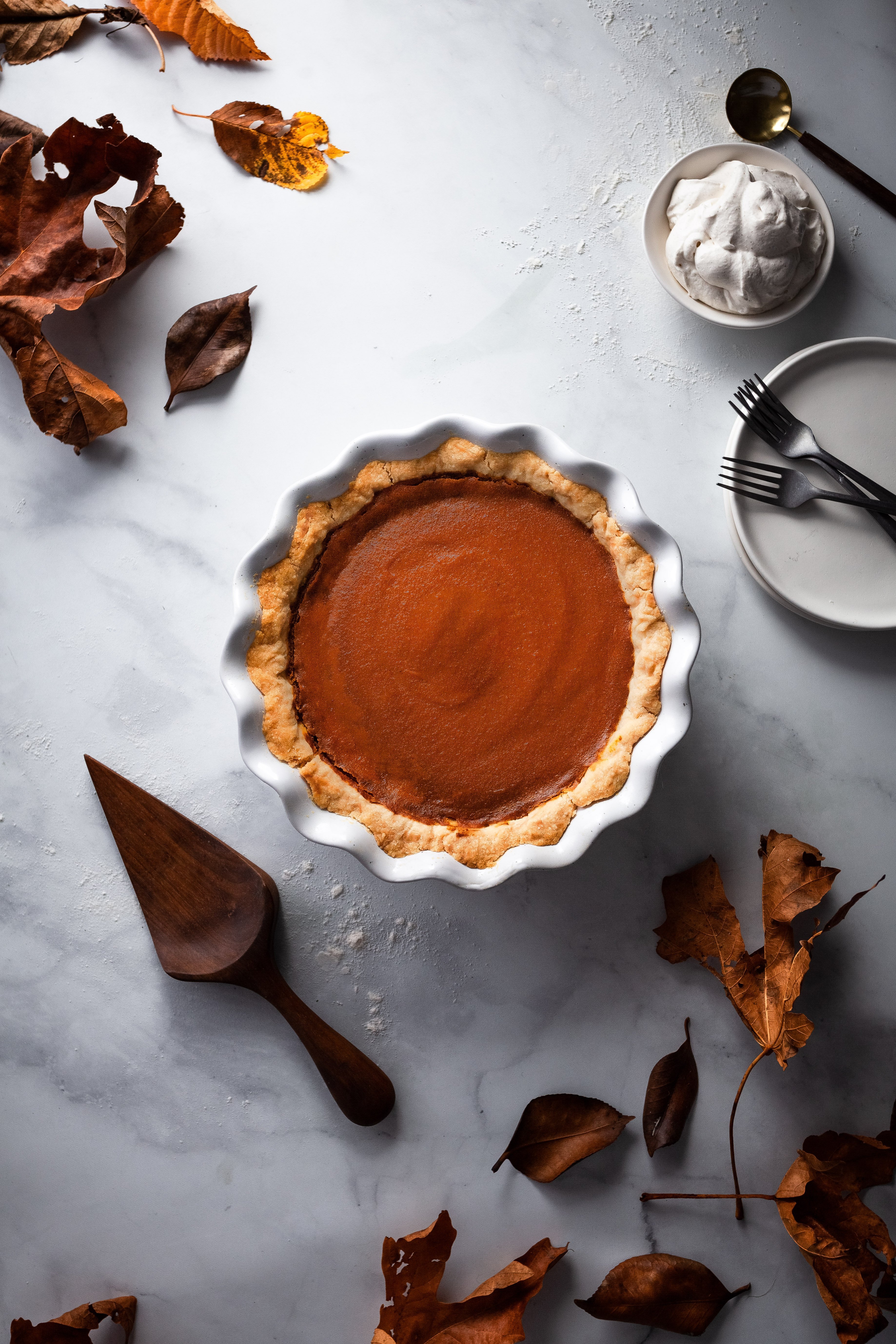 overhead image of vegan pumpkin pie with fall leaves and a pie lifter.
