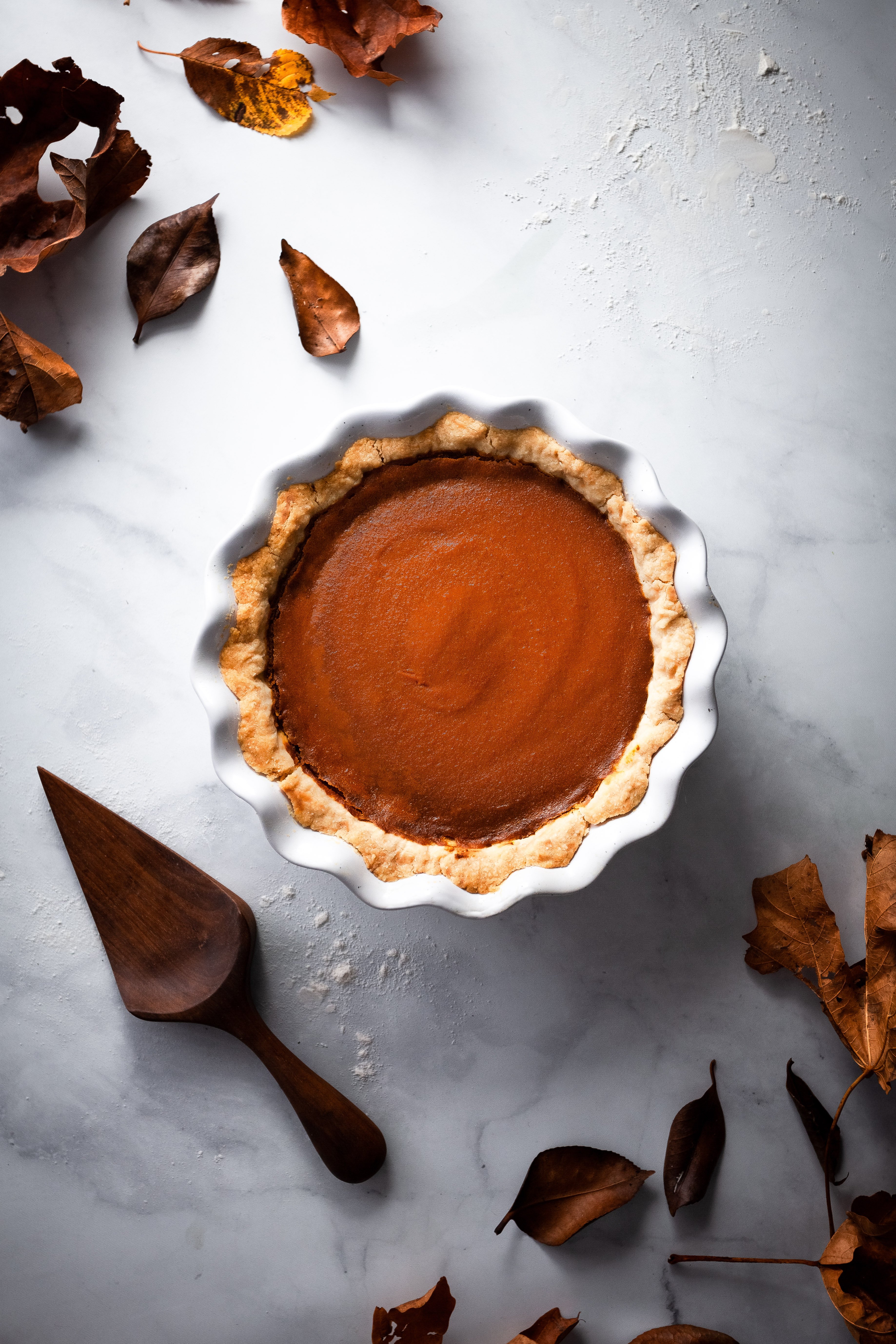 overhead image of pumpkin pie with fall leaves and a pie lifter.