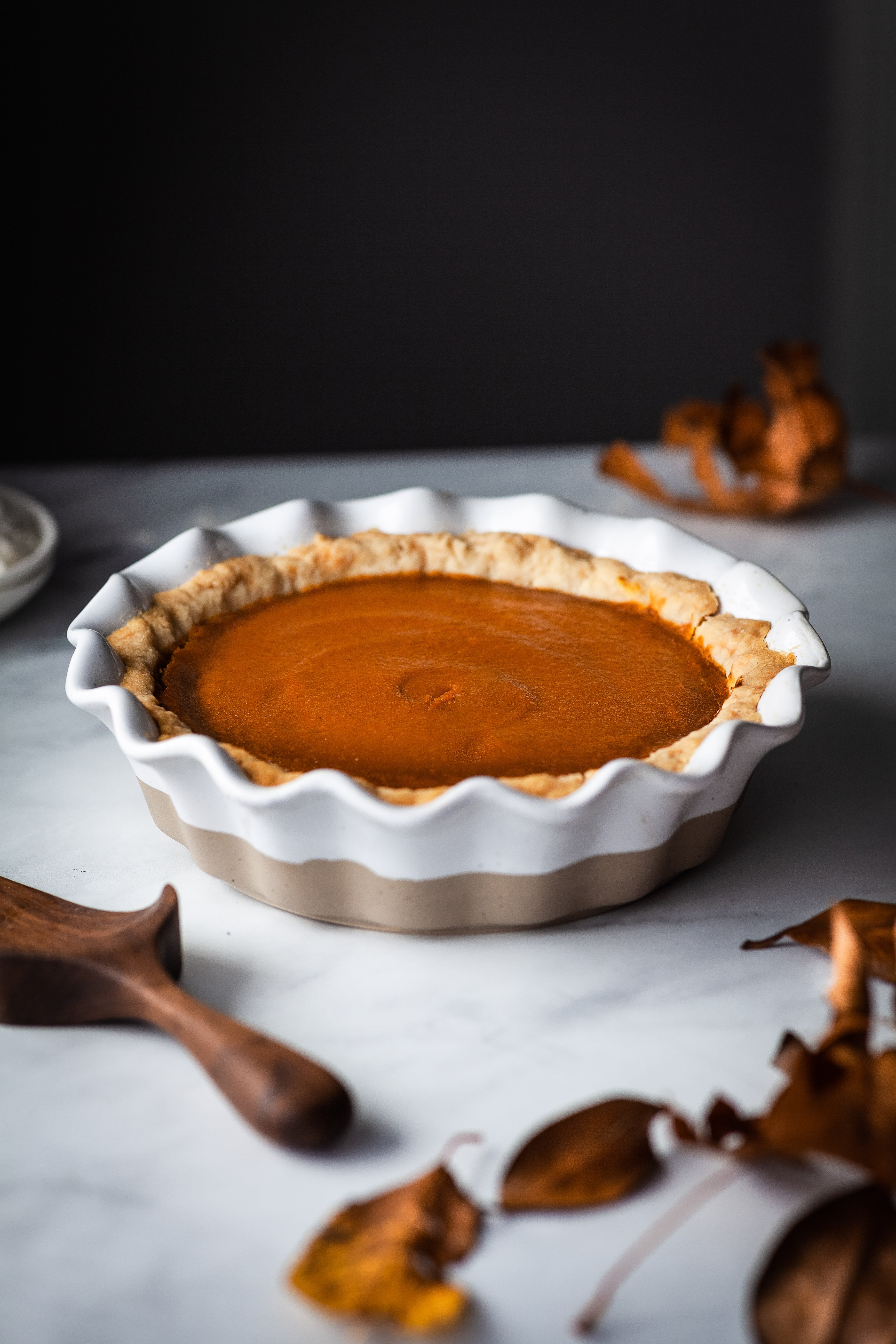 head on image of vegan pumpkin pie in a white pie plate and fall leaves in the foreground.
