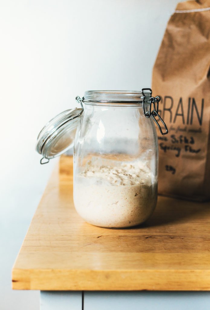 a head on image of a glass jar of sourdough starter on a wooden surface.