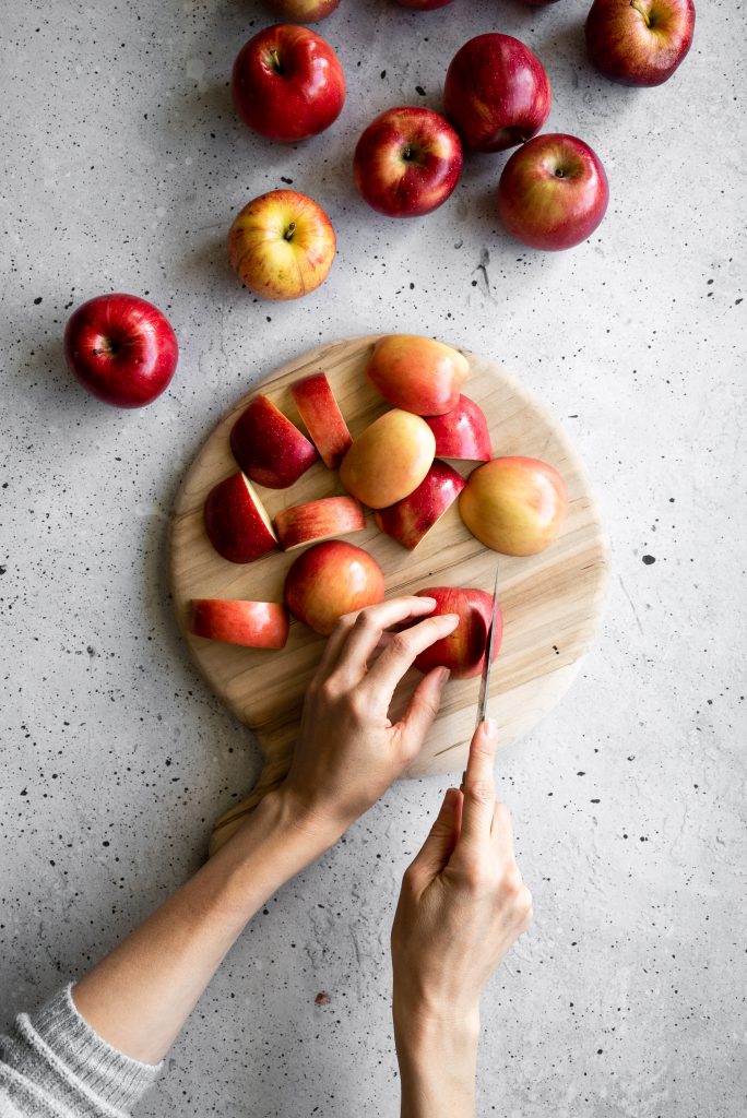 overhead image of a person slicing apples on a cutting board.