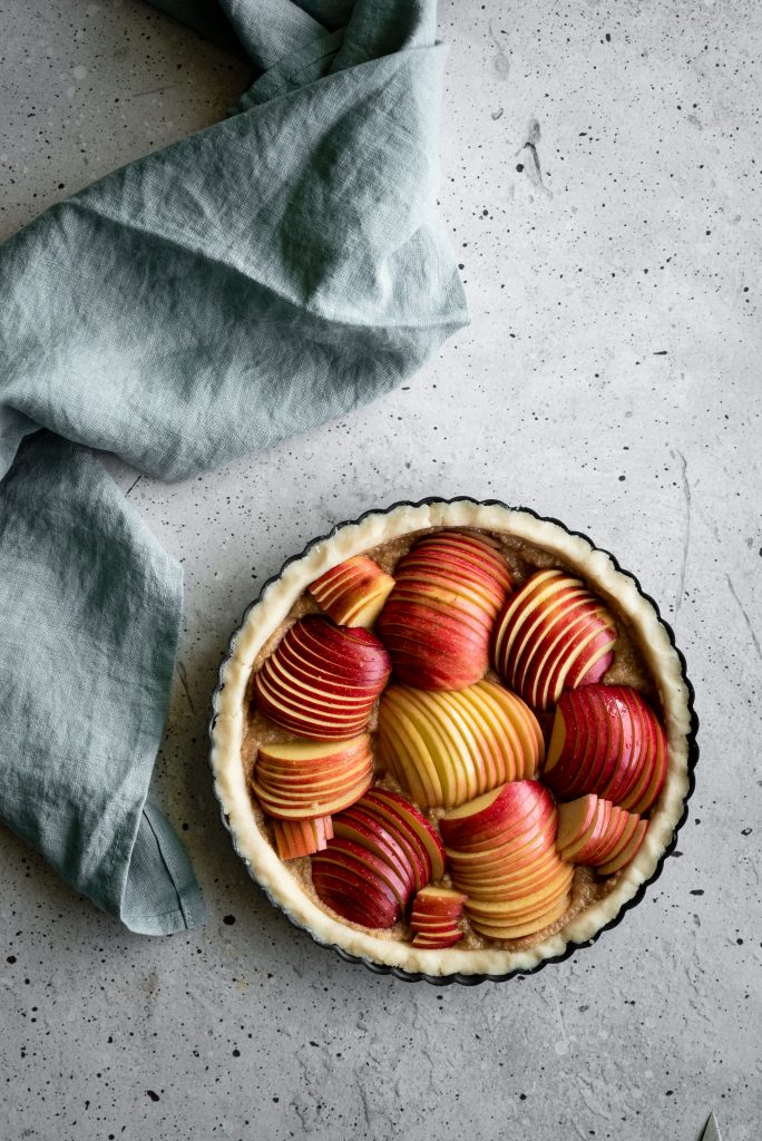 overhrad image of an unbaked apple tart with a blue linen on the left.
