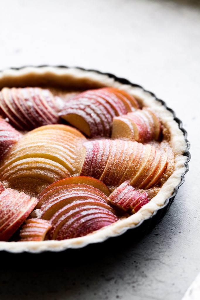 angled close up on an unbaked apple tart coated in sugar.