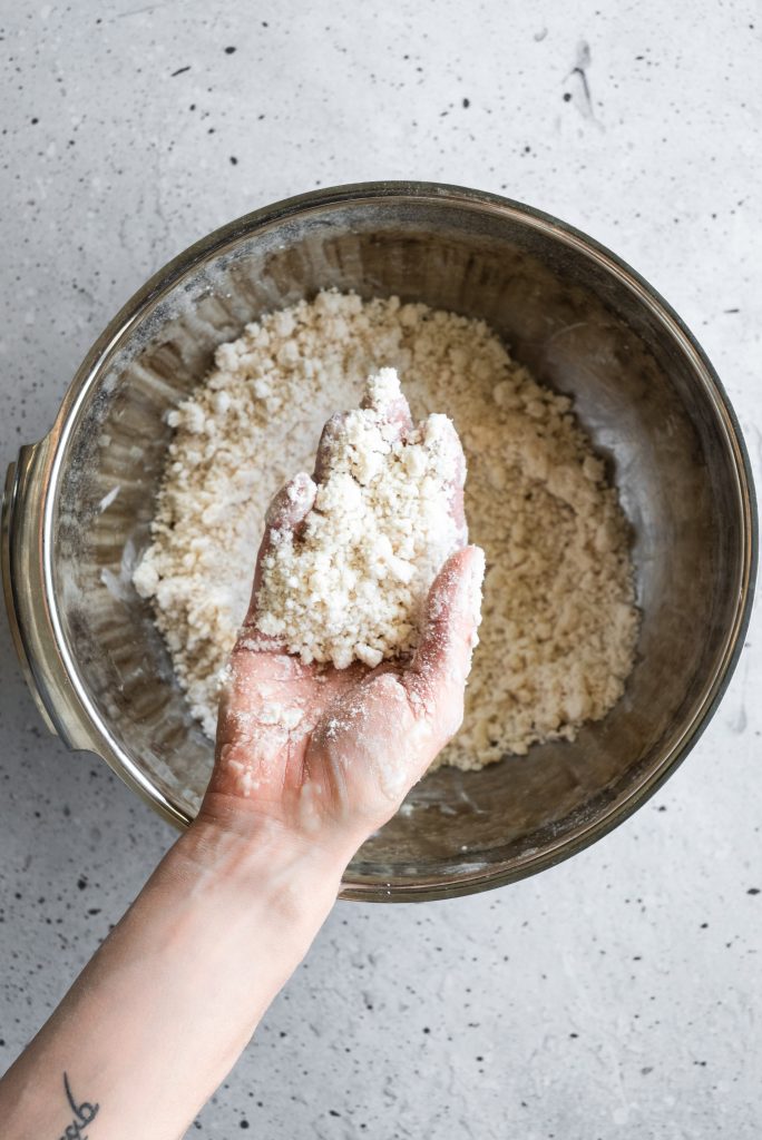 overhead image of a hand holding pastry dough overtop of a large bowl of dough.
