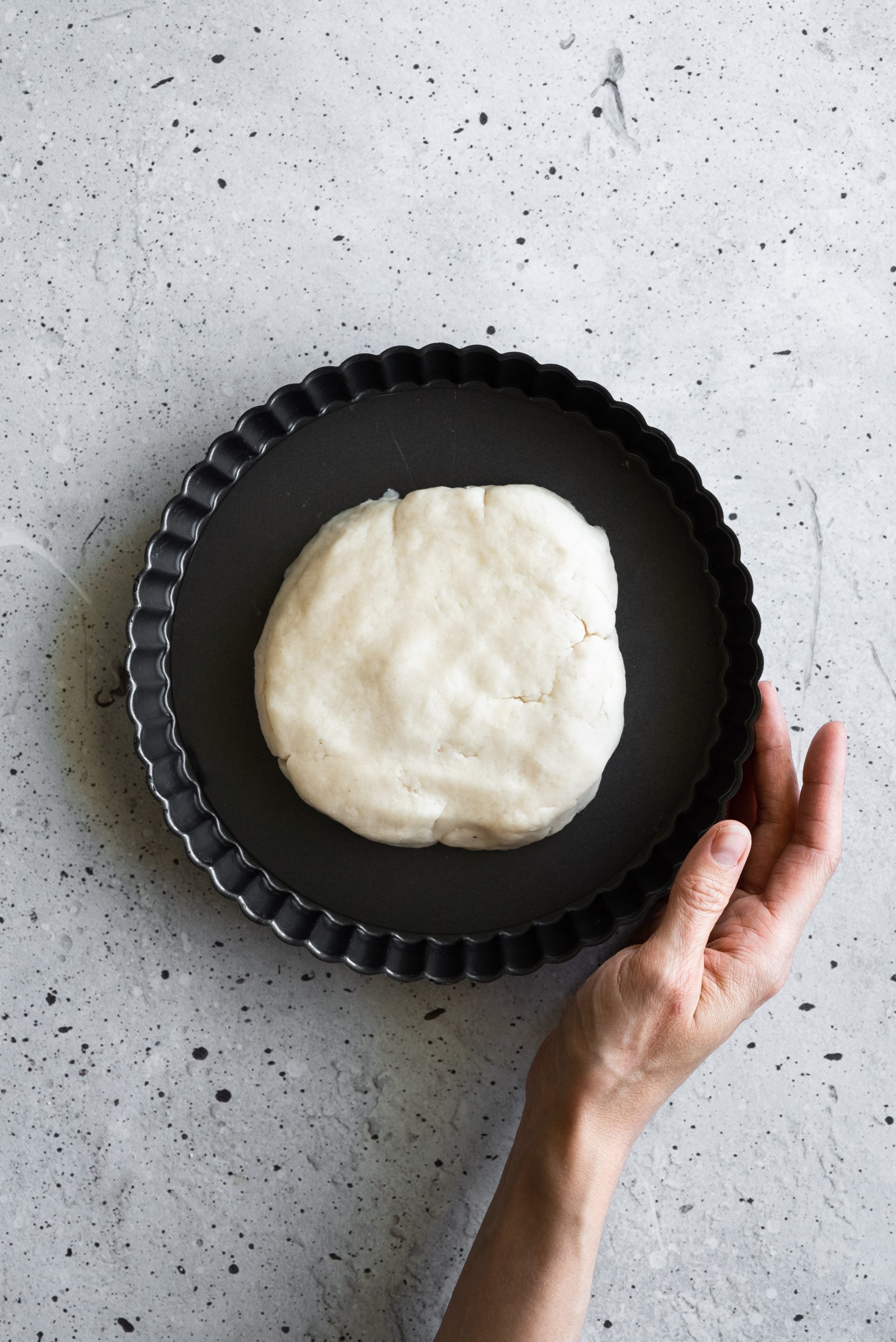 overhead image of tart dough in the middle of a tart pan with a hand holding the pan.
