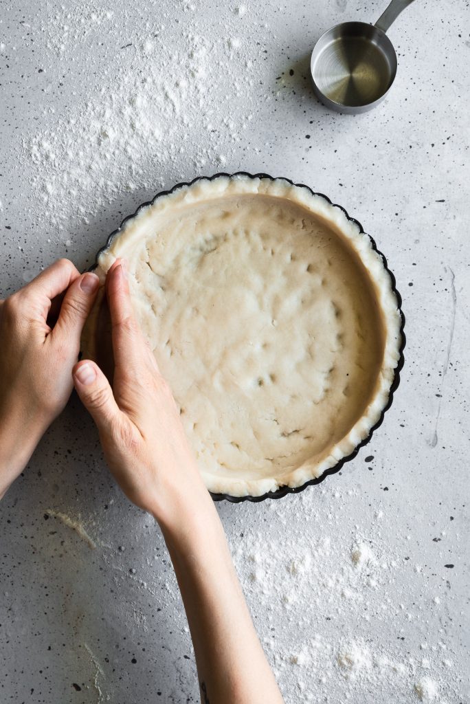 overhead image of two hands pressing tart dough into a tart pan.