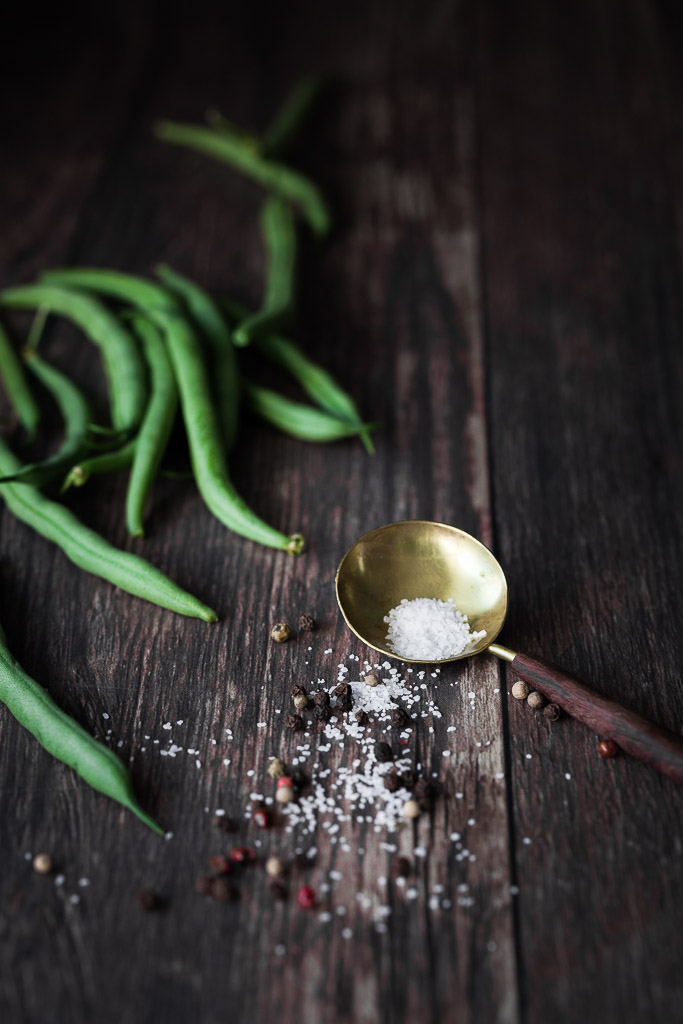 closeup image of a golen spoon with pickling salt, peppercorns and green beans.