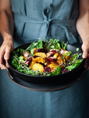 A person in a blue apron holding a bowl of roasted beet salad.