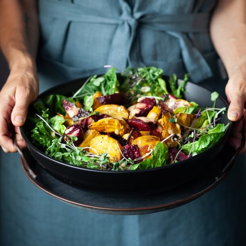 A person in a blue apron holding a bowl of roasted beet salad.