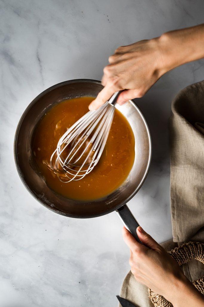 overhead view of a baker whisking caramel in a skillet.