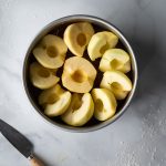 overhead view of apple halves arranged in a round cake pan with a knife on the left.