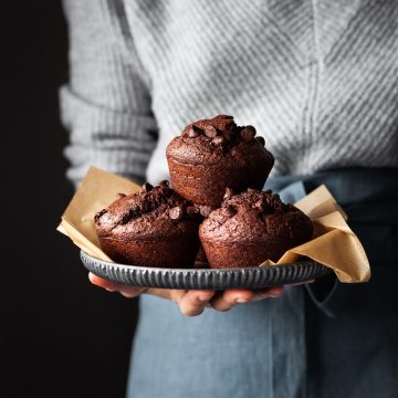 a baker in a grey sweater holding a tray with 3 chocolate beet muffins.