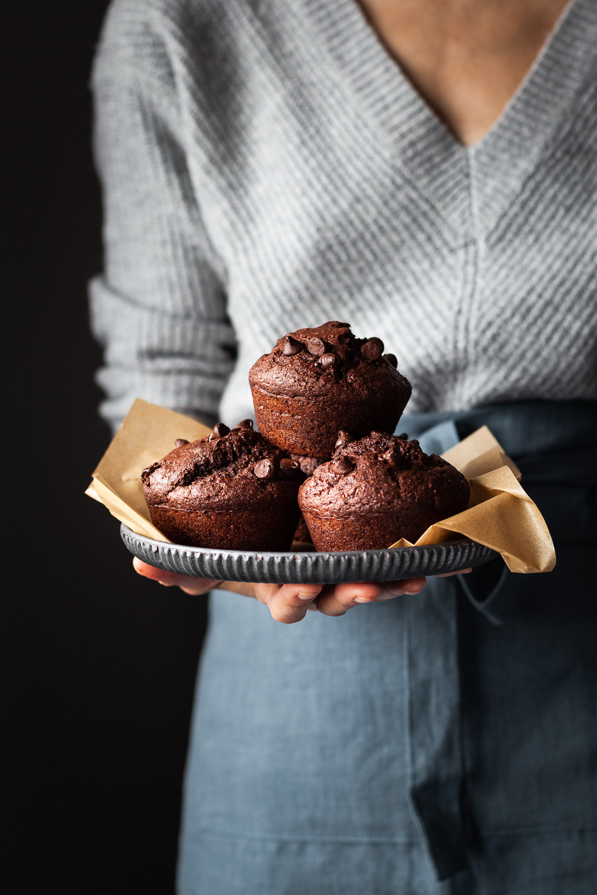 a baker in a grey sweater holding a tray with 3 chocolate beet muffins.