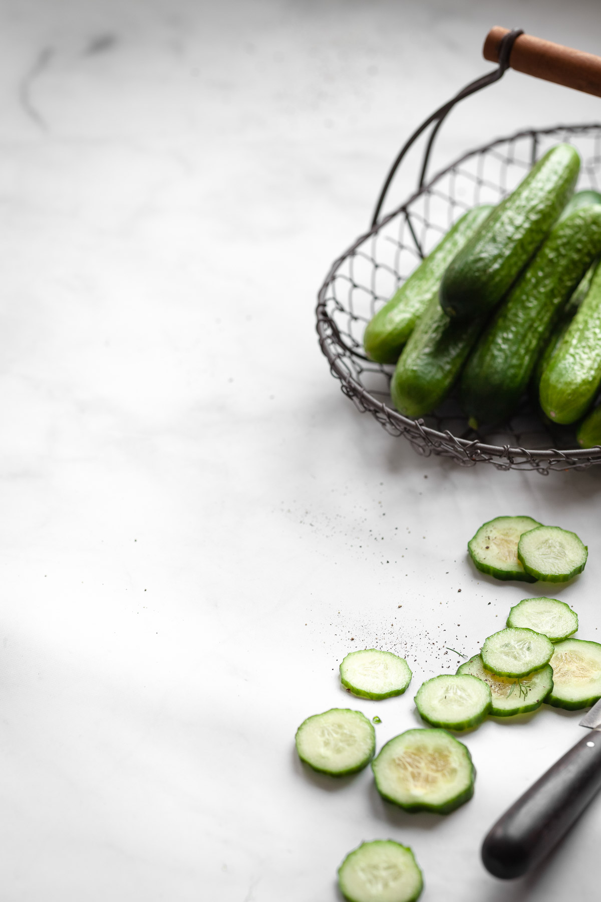 Side view of a wire basket with cucumbers and cucumber slices.