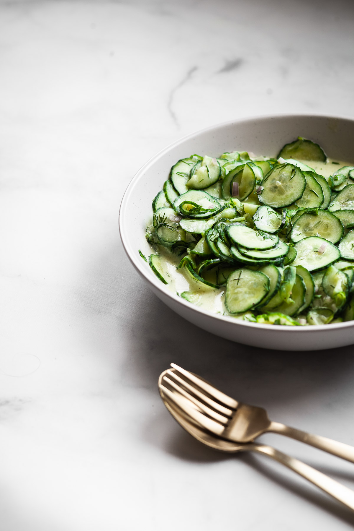 Side view of a large bowl of vegan German cucumber salad with gold serve ware.