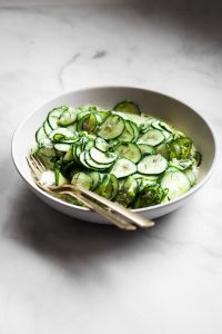 Side view of a large bowl of vegan German cucumber salad with gold serve ware.