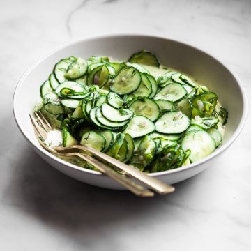Side view of a large bowl of vegan German cucumber salad with gold serve ware.
