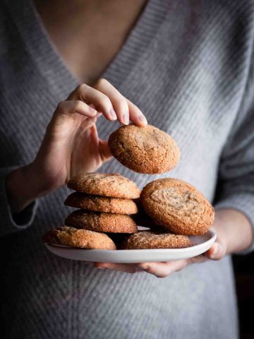 a person in a grey sweater holding a plate of vegan ginger spice cookies.