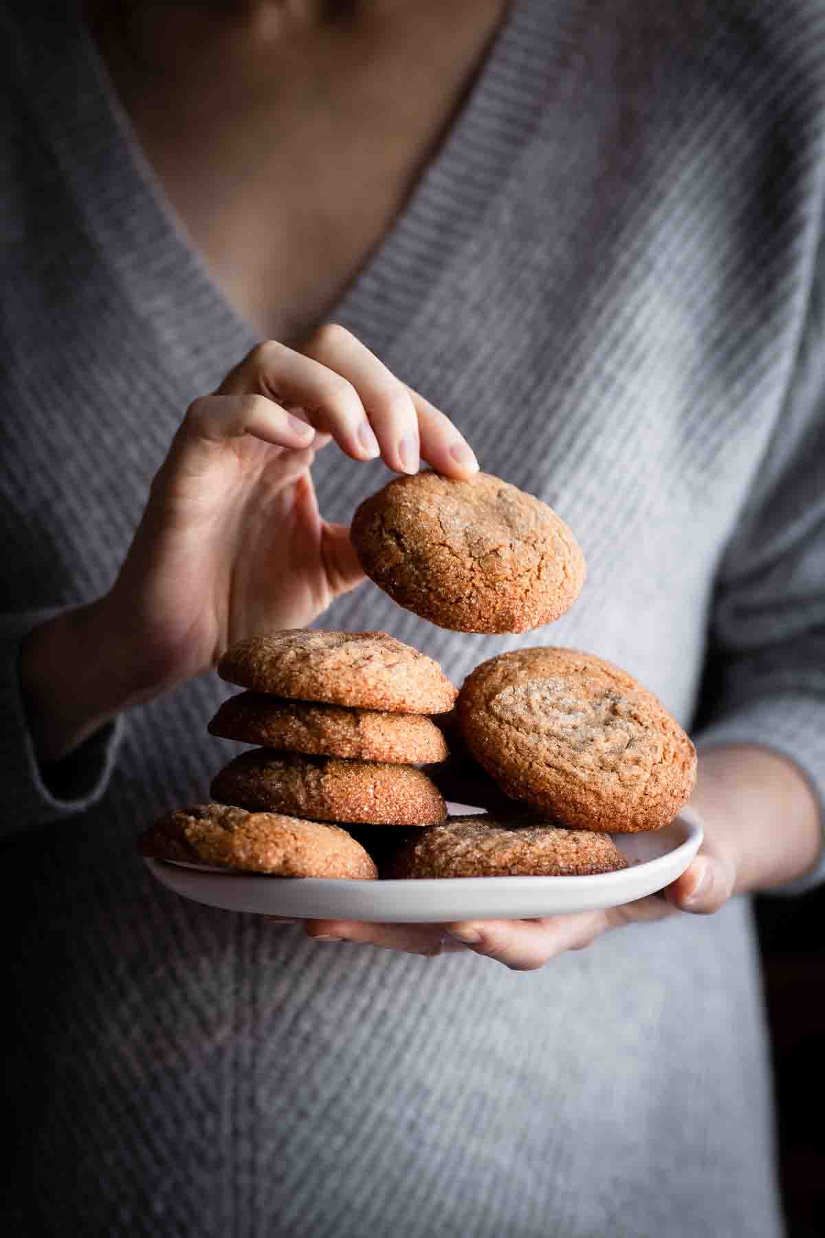 a person in a grey sweater holding a plate of vegan ginger spice cookies.