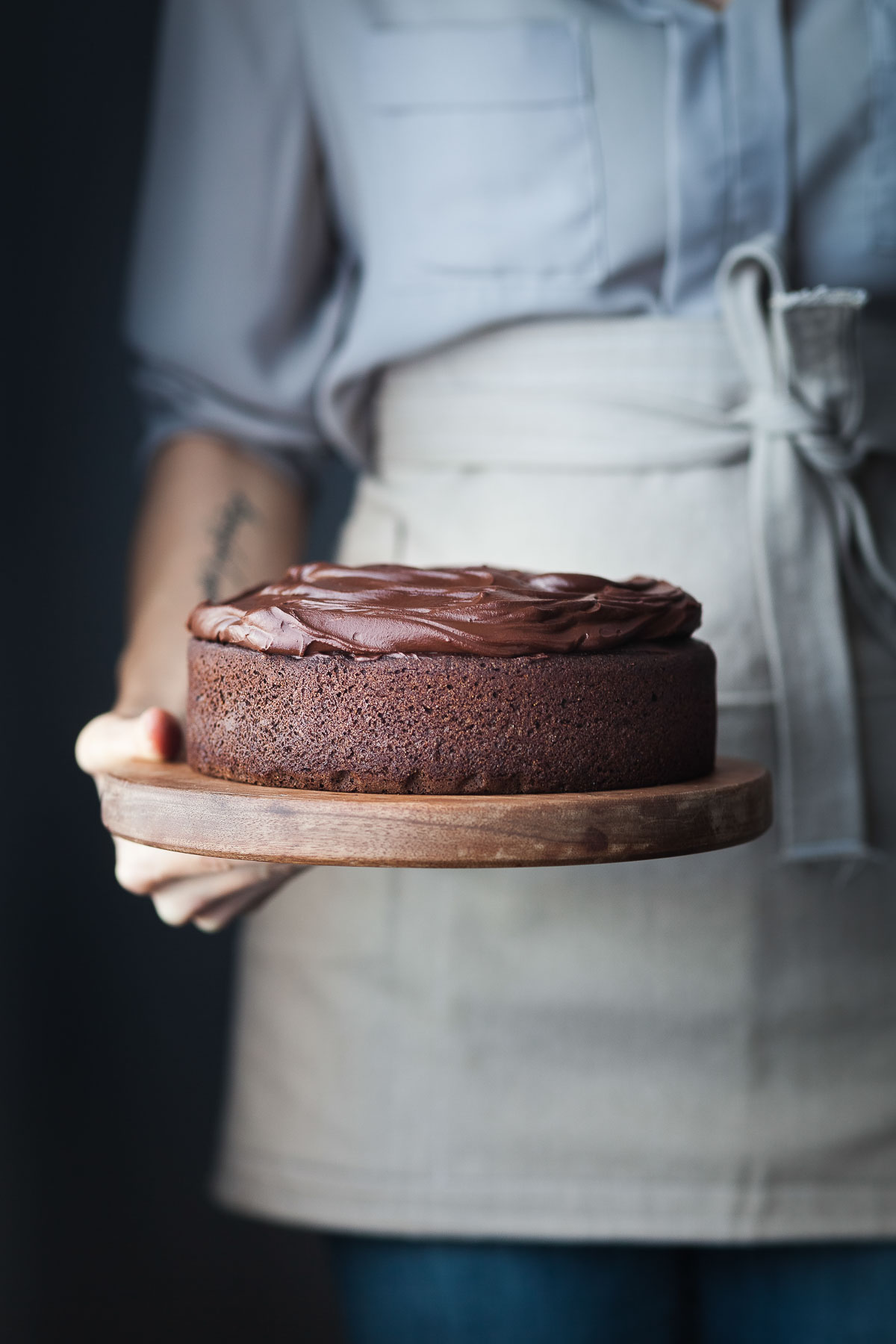 a baker in an apron holding a frosted chocolate beet cake. 