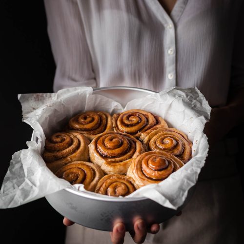 a baker holding a tin of vegan cinnamon rolls.