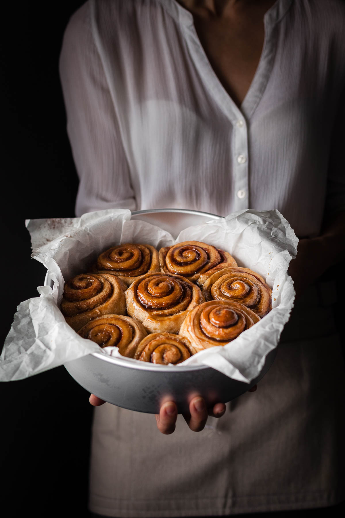 a baker holding a tin of vegan cinnamon rolls.