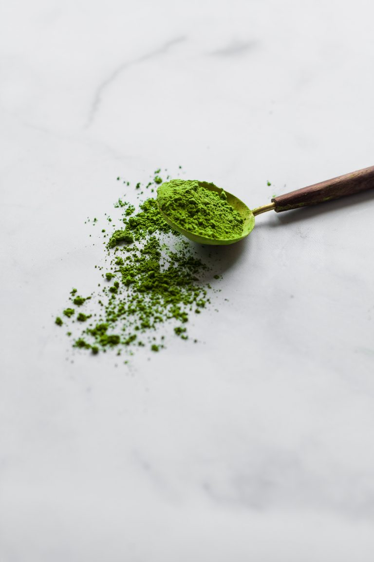 closeup view of a spoon of matcha tea on a marble surface.